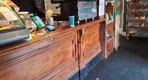 Inside the shop: an antique carved wooden counter with a coffee machine, and shelves of freshly baked bread behind it.
